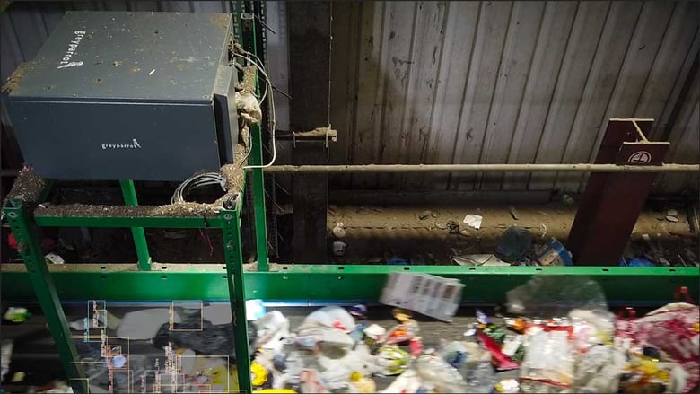 A Greyparrot monitoring unit sitting above a recovery facility conveyor belt covered in plastic waste
